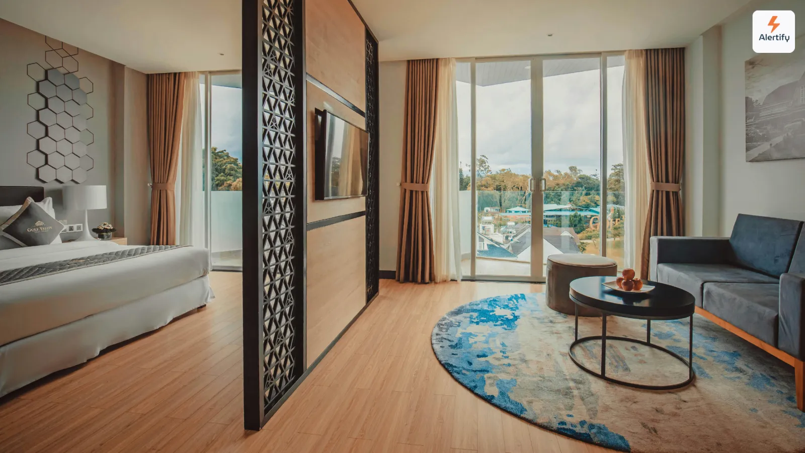 Modern short-term rental suite with a made bed, blue sofa and floor-to-ceiling balcony windows