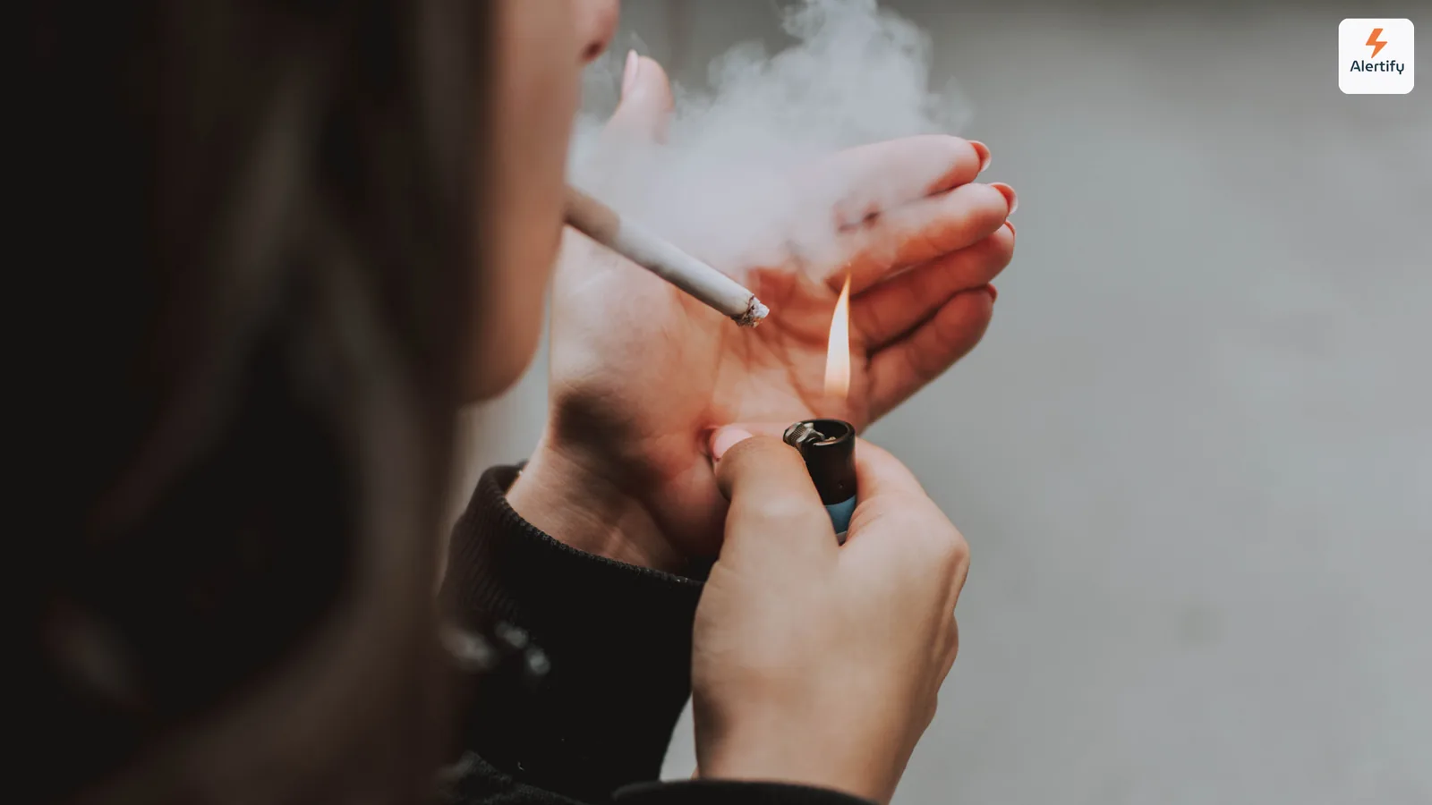 Person lighting a cigarette indoors with smoke curling around their hands