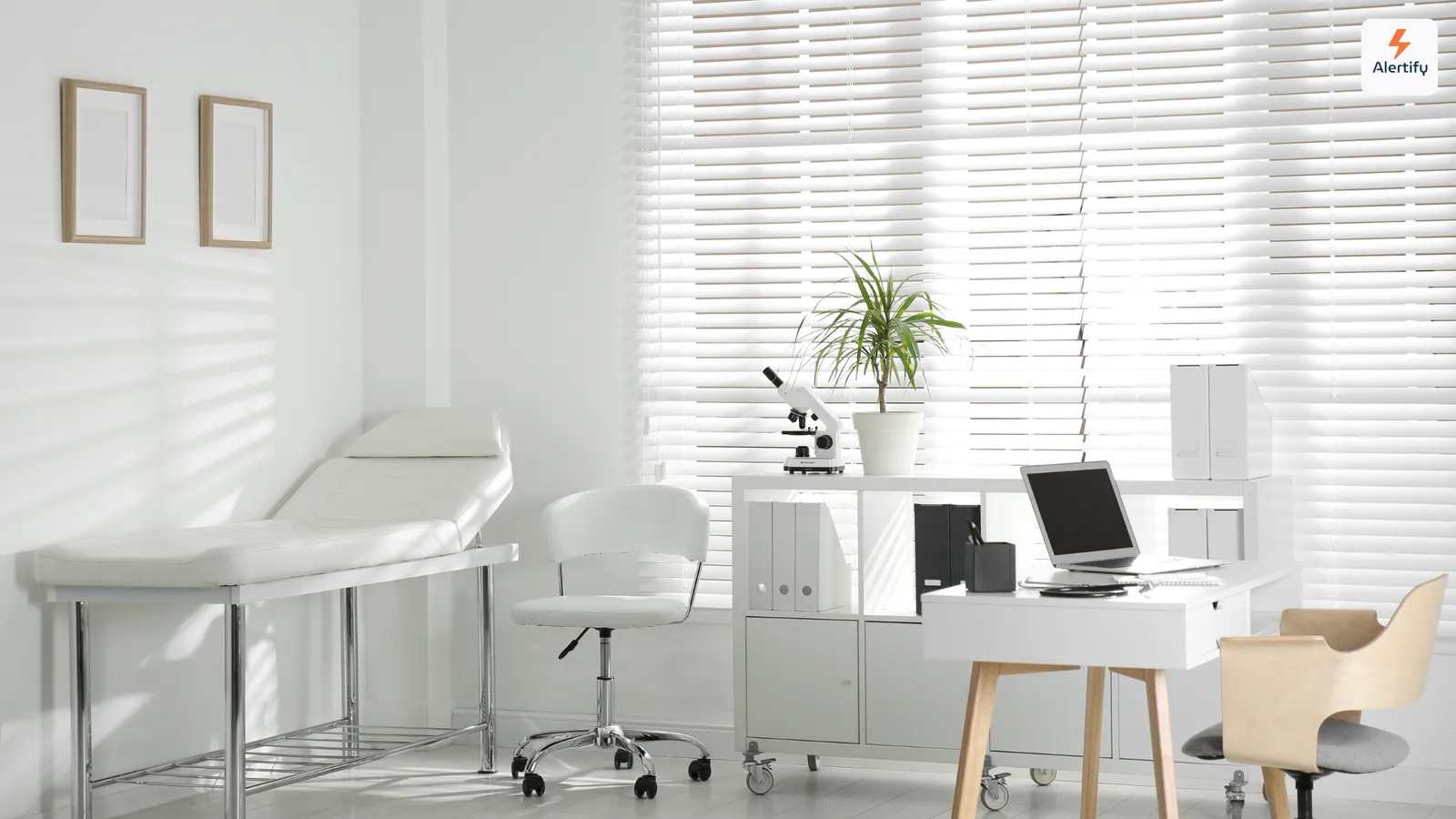 Empty clinic room with an examination couch, a desk with a laptop and window blinds