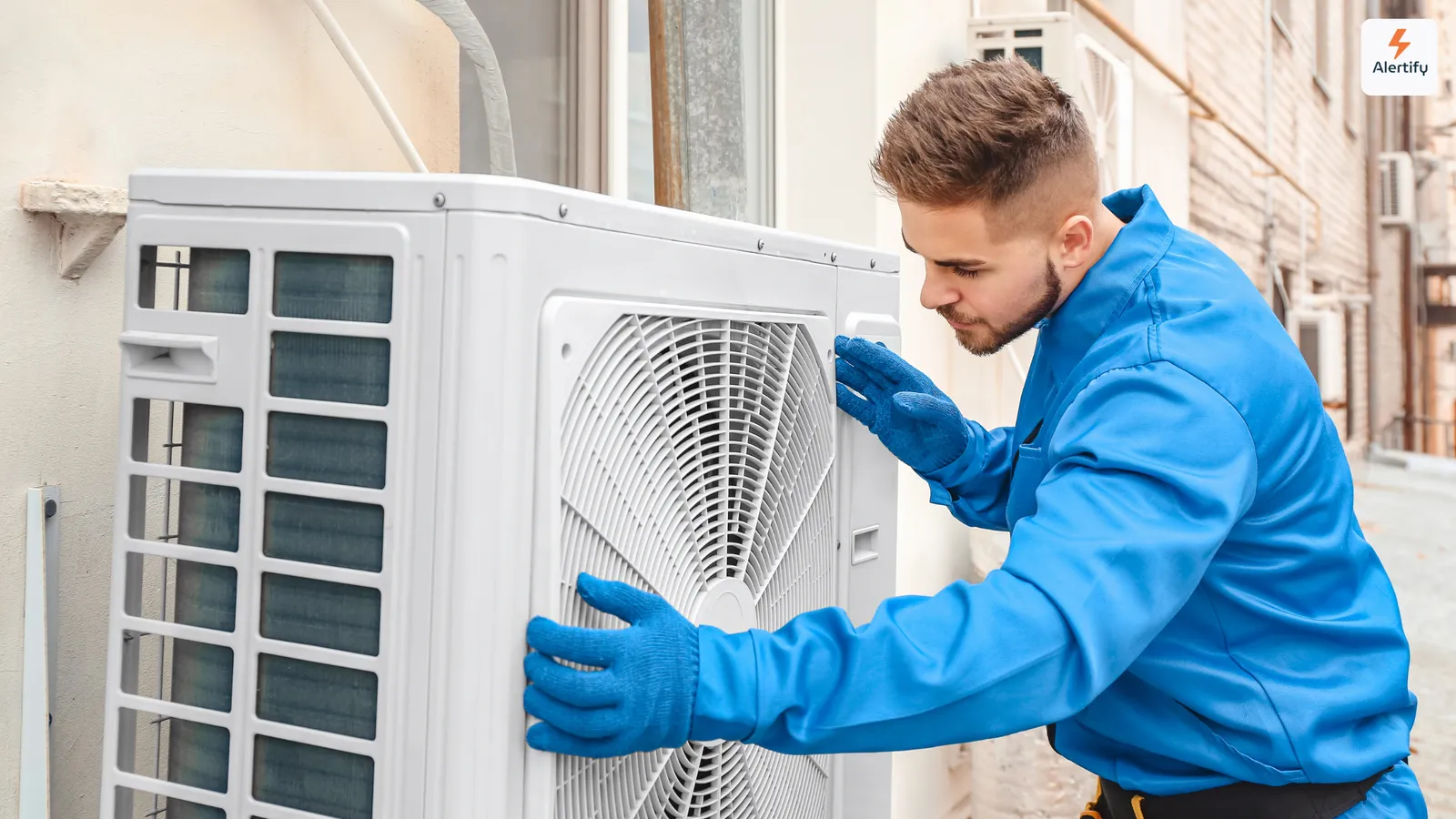 HVAC technician in blue overalls and gloves servicing an outdoor air conditioning unit