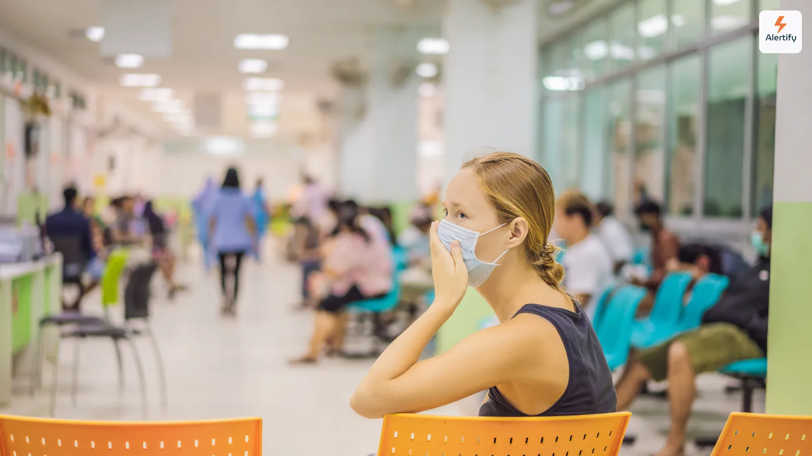 Woman wearing a face mask seated in a busy hospital waiting area