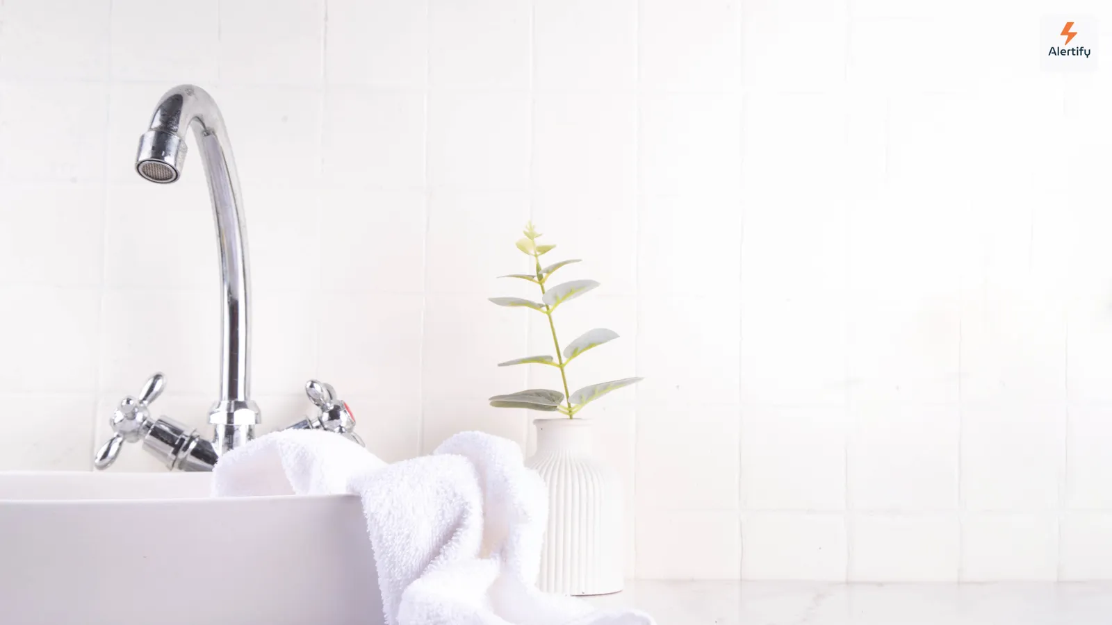 A bright white-tiled bathroom with a basin, a folded towel and a small potted plant — the kind of humid room where mold takes hold first.