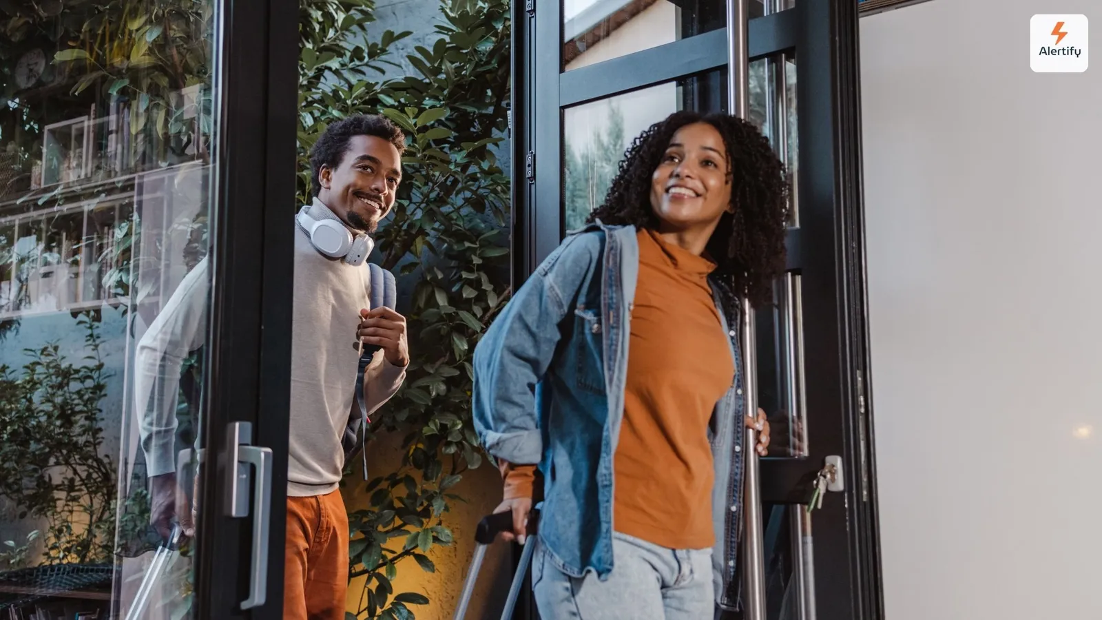 Two guests arriving at a rental with wheeled luggage, smiling as they come through a glass door.