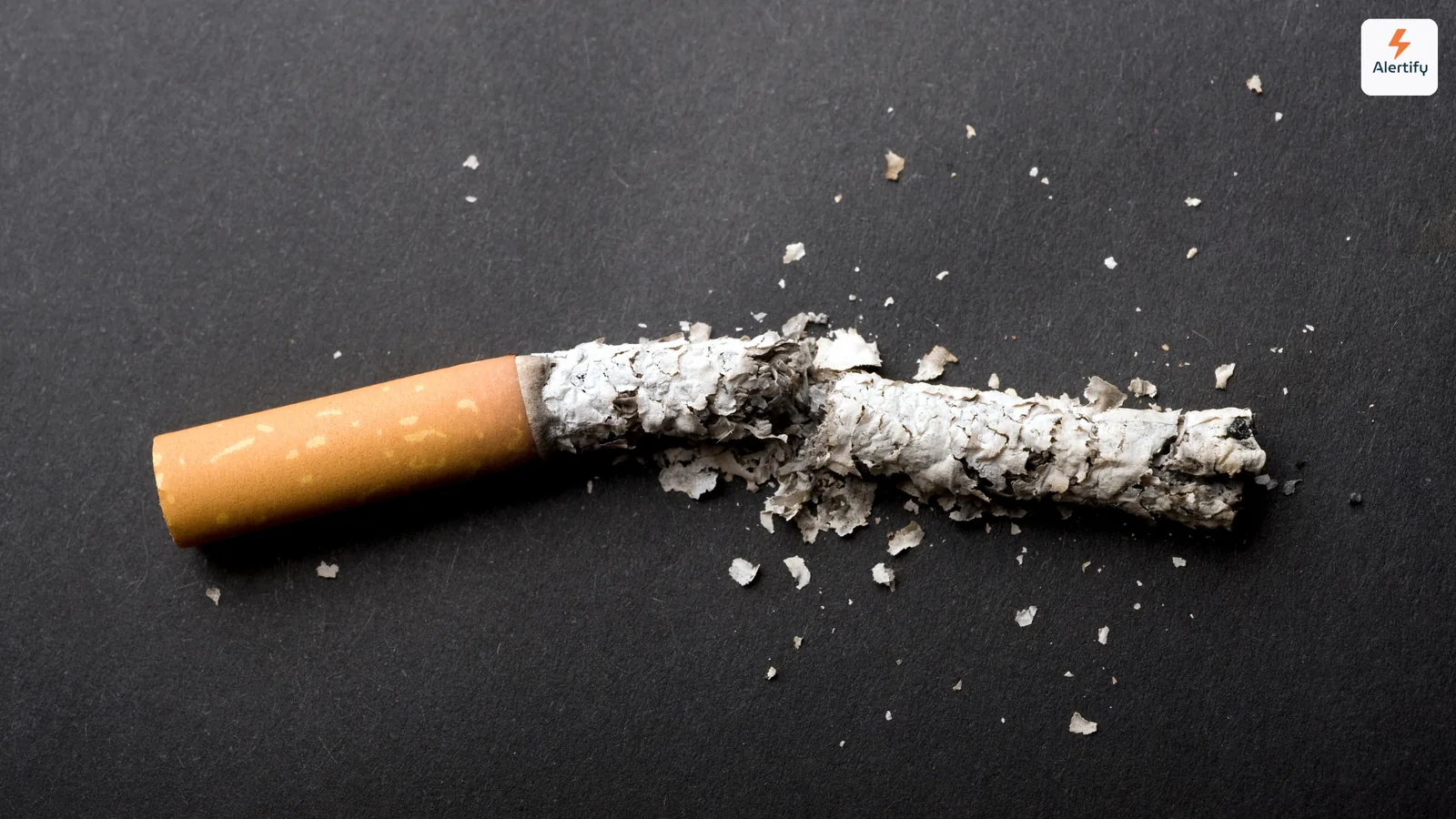Broken cigarette snapped in half with ash scattered across a dark surface